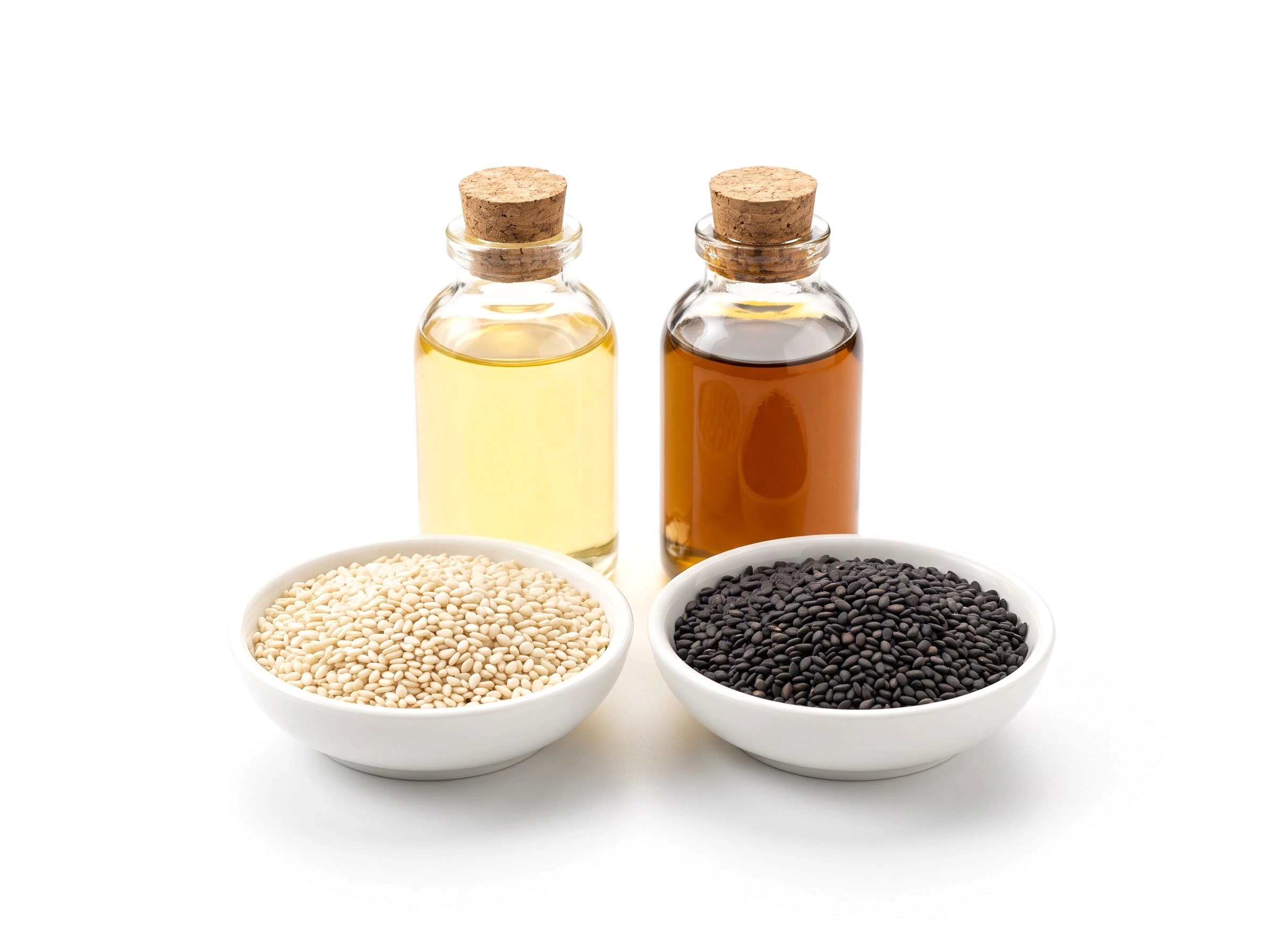 Small bowls of white and black sesame seeds beside two bottles of cold-pressed oil